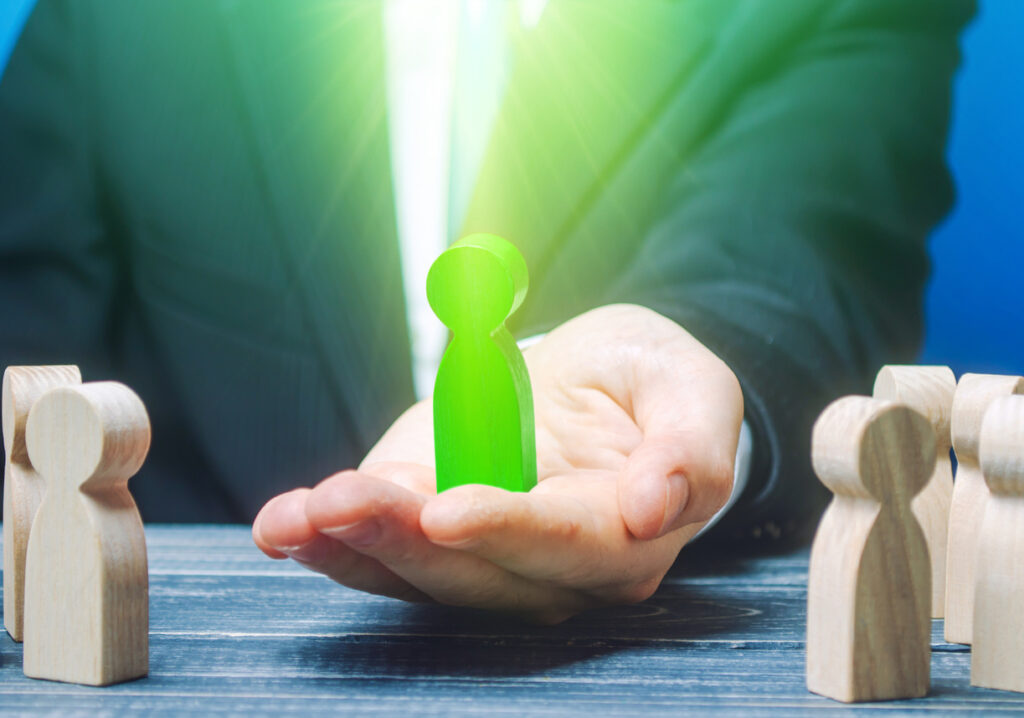 a man holding a green wooden person piece to depict attracting qualified candidates