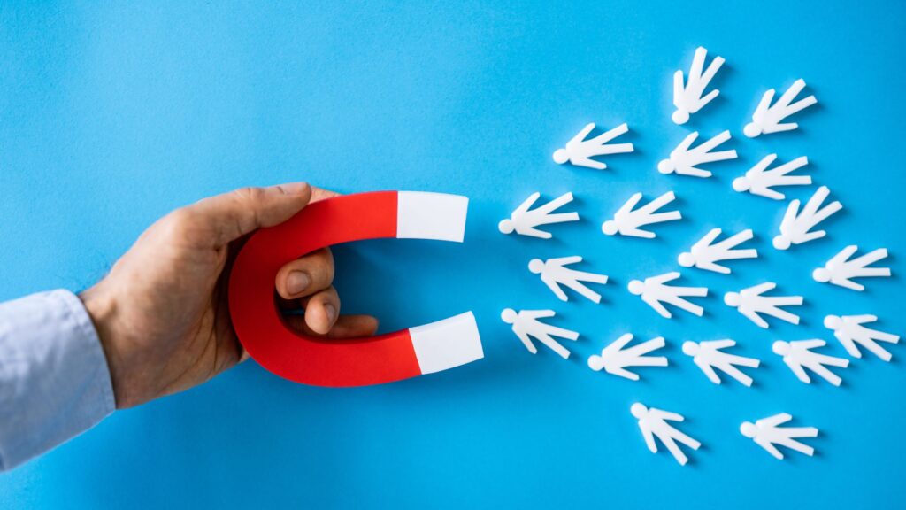 a man holding a magnet attracting cutouts of people to signify attracting talents through interviewing and assessment techniques