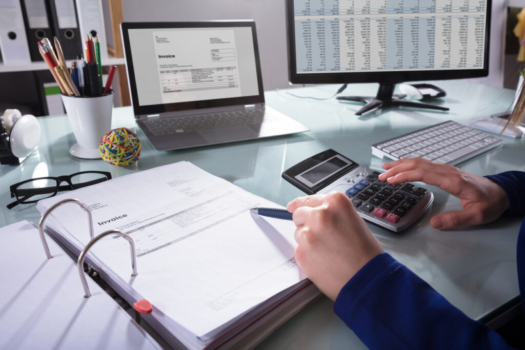 Close-up Of A Businessperson's Hand Calculating remote taxes At Workplace