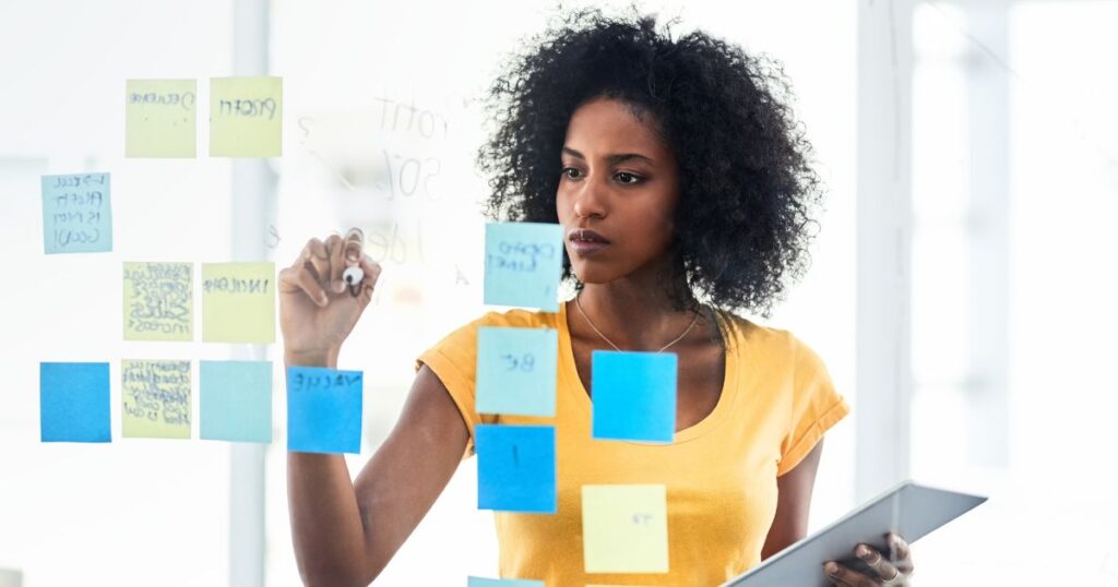 woman writing on a glass board with sticky notes about remote work goals and expectations