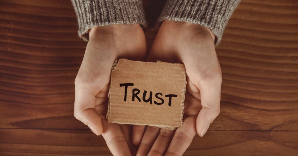 woman's hands with a piece of carton with the word "trust" written on it to signify trust in remote work